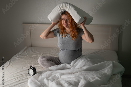 Caucasian pregnant woman sits in bed, holds a pillow on her head and cries. Insomnia. photo