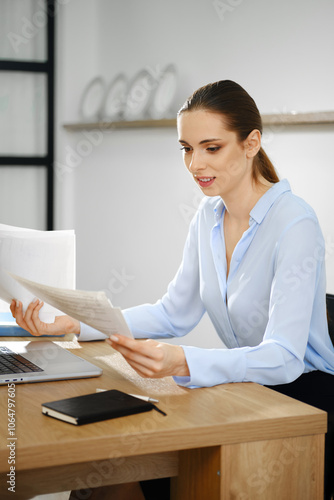 A business woman reviews documents at her desk in a modern office space during the workday