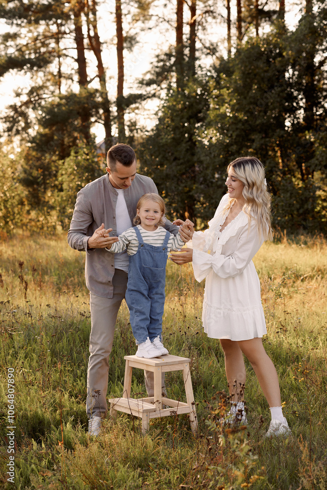 Fototapeta premium Happy Caucasian family of three, man, woman and child happy in the field in summer. Casual clothes. Mom blonde with long hair in a white dress.