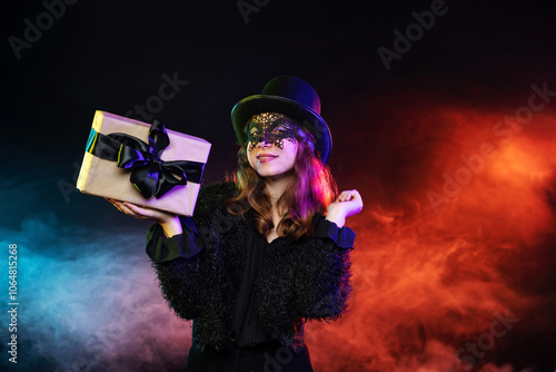 Young woman wearing black hat, mask, clothes holds gift with black bow on darkness background with magical colorful smoke. Banner, poster, copy space. Black friday sale, halloween party,