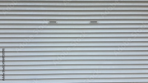 Photograph of the old rolling door taken from the front side. The texture of a silver shutter metal door. Factory gate.