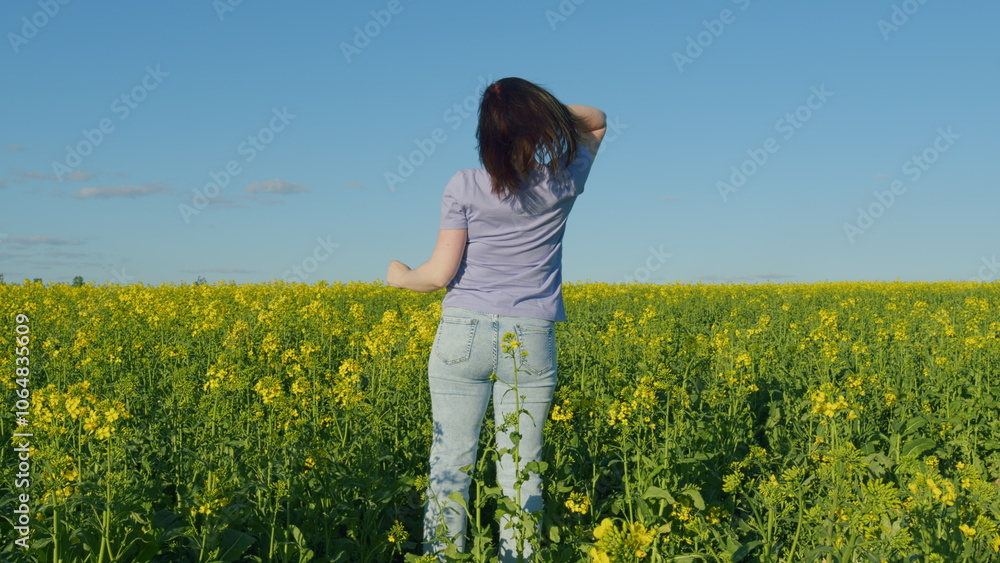 Woman In A T-Shirt Standing In A Flowering Canola Rapeseed Field. Pretty Young Woman With Arms Raised In Air In Rapeseed Field. Woman In A T-Shirt Standing In A Flowering Canola Rapeseed Field. Pretty Young Woman With Arms Raised In Air In Rapeseed Field.