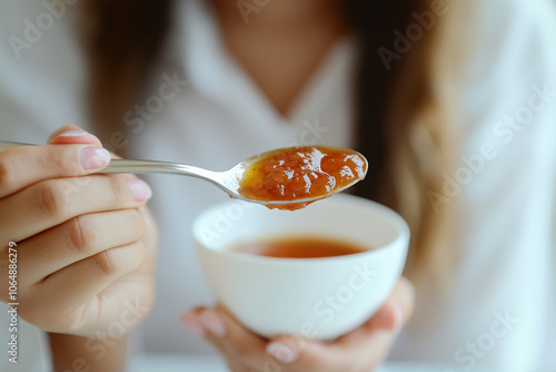 Hand holding spoon with sweet fruit jam close to white bowl, focus on textured spread, breakfast food concept photo