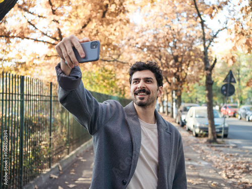 Closeup portrait of young smiling middle eastern man taking selfie with phone on a beautiful autumn day. 