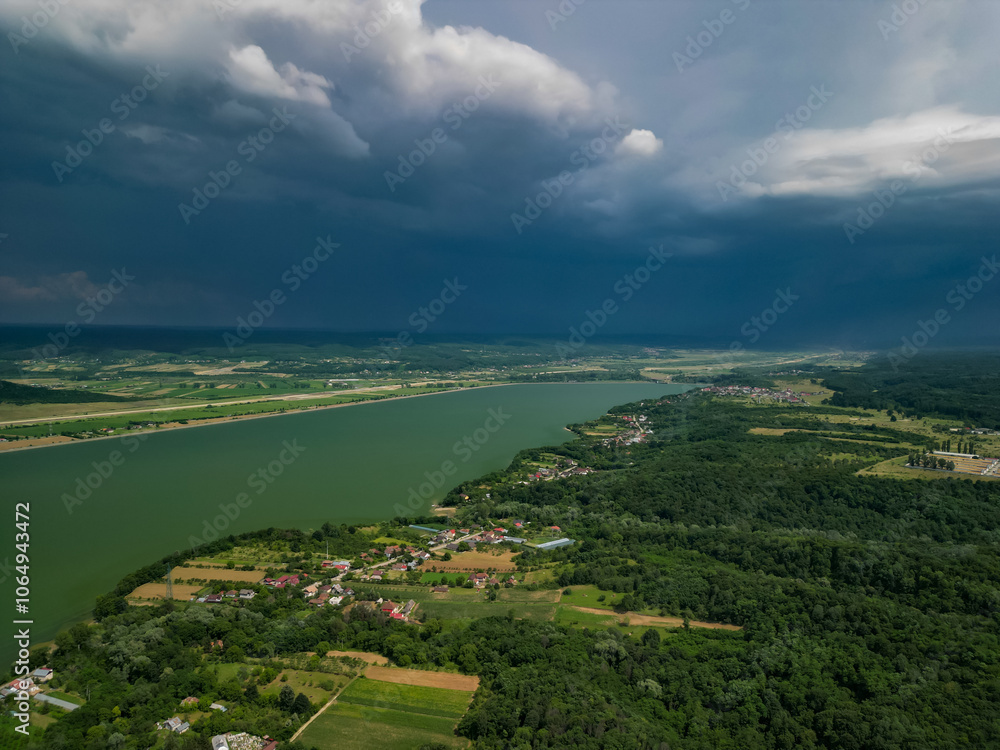 Obraz premium Panorama with a storage dam captur with a drone in the countryside. A calm river that comes from the mountains among the green forests and flows into the lake at the edge of a village in Romania