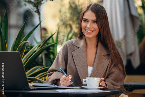 Happy smile, sitting. Beautiful young woman is outdoors of the restaurant by the table