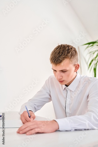 Portrait of a high school student in a white uniform doing homework, sitting at a table with textbooks, writing in a notebook