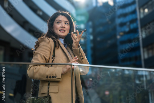 Young confident businesswoman sending voice message on smart phone on the street. Business female, design professional occupation, talking to the phone microphone, send voicemail to colleagues. photo