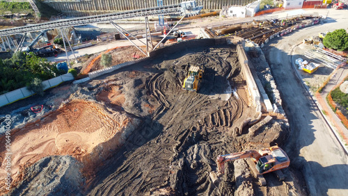 Imagem aérea de uma área de construção industrial com grandes caminhões e guindastes, destacando a movimentação no solo. photo