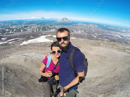 two tourists a married couple a young woman and a young man white travel around Kamchatka, take pictures on an action camera against the backdrop of a volcano photo