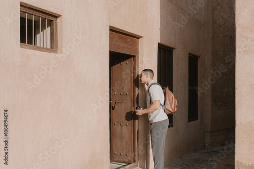 Young arab man in old city in Dubai. Solo male traveler with a backpack and coffee exploring streets early in the morning