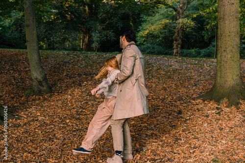 Mediterranean father holds his adorable red-haired daughter under her armpits and spins her around in autumn park