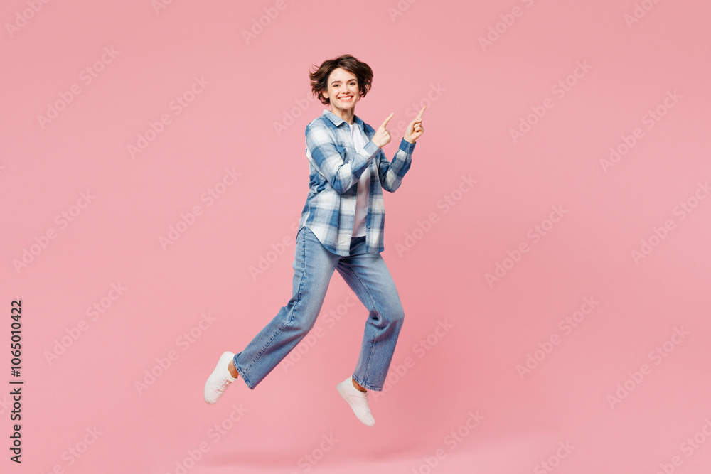 Full body young woman wear blue shirt white t-shirt casual clothes jump high point index finger aside on area mock up isolated on plain pastel light pink background studio portrait. Lifestyle concept. Full body young woman wear blue shirt white t-shirt casual clothes jump high point index finger aside on area mock up isolated on plain pastel light pink background studio portrait. Lifestyle concept.