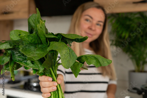 Foto Young woman holding fresh spinach in a modern kitchen while preparing a healthy