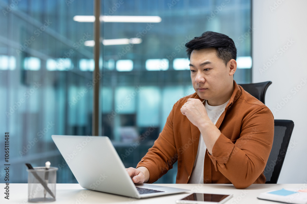 Asian man businessman working in modern office, focused on laptop. Casual attire signifies balance between professionalism and comfort, surrounded by large windows enhancing open workspace. Asian man businessman working in modern office, focused on laptop. Casual attire signifies balance between professionalism and comfort, surrounded by large windows enhancing open workspace.