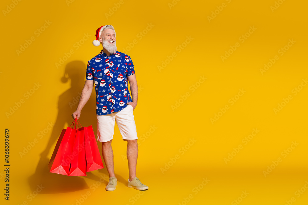 Fototapeta premium Full body portrait of stylish santa mall bags look empty space wear christmas print shirt isolated on yellow color background