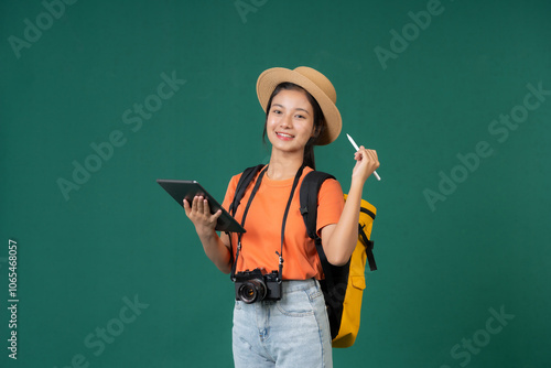 Asian female tourist enjoying summer vacation, wearing a hat and working with a laptop, holding a camera and taking pictures in the studio, intending to record the memories of this trip.