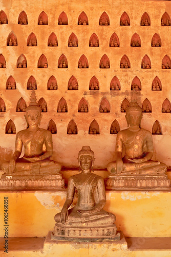 Three buddha statues in front of a wall filled with many miniature buddha figurines in the cloister wall of Wat Si Saket, a buddhist temple in Vientiane, Laos photo