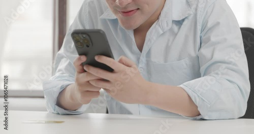 Close-up of an Asian man reading a message on his smartphone with a joyful expression, capturing a moment of happiness and digital connection