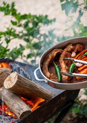 Grillfleisch in einer Aluminiumschüssel mit Grillzange und Feuer