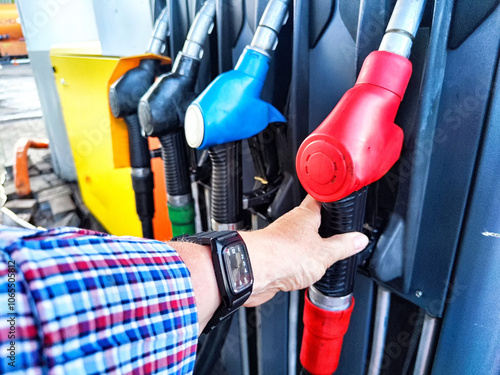 A person refuels their car with a red fuel nozzle at a service station in the early morning light