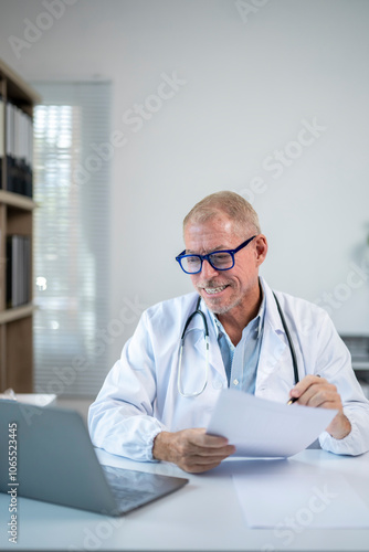 Senior doctor smiling and working on laptop in medical office