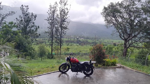 A wide view of a superbike parked outside a house in heavy rain at a hill station in Karnataka