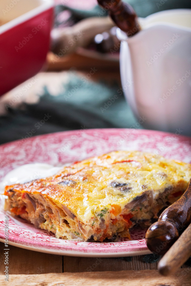 Oven baked omelette with vegetables served with sour cream on wooden background.