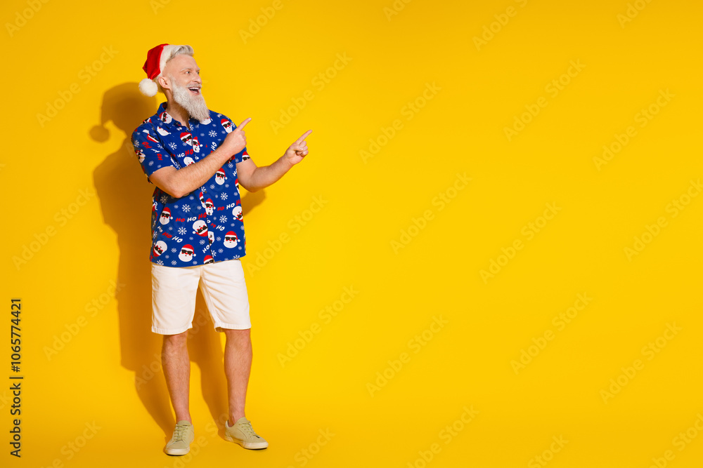 Full body portrait of stylish santa direct fingers empty space new year xmas print shirt isolated on yellow color background Full body portrait of stylish santa direct fingers empty space new year xmas print shirt isolated on yellow color background
