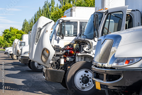 Middle duty white day cab rigs semi trucks with box trailers standing in row with open hoods for engine maintenance and inspection photo