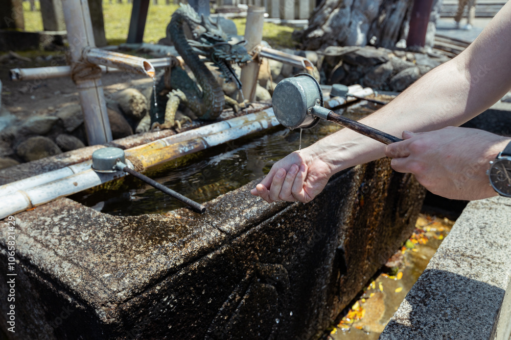 A tourist is holding a ladle of water to wash his hands before going to a shrine in Japan as a purification ritual
