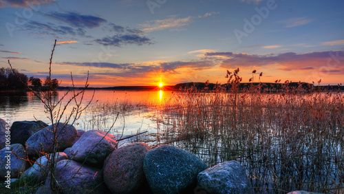 sunset on the lake , rocks in the foreground and calm water