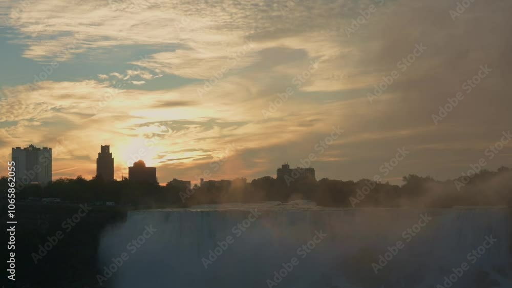 breathtaking view of the sunrise casting a warm glow over Niagara Falls, with mist rising and silhouetted buildings in the distance. Captures the serene beauty of dawn at this iconic location. breathtaking view of the sunrise casting a warm glow over Niagara Falls, with mist rising and silhouetted buildings in the distance. Captures the serene beauty of dawn at this iconic location.