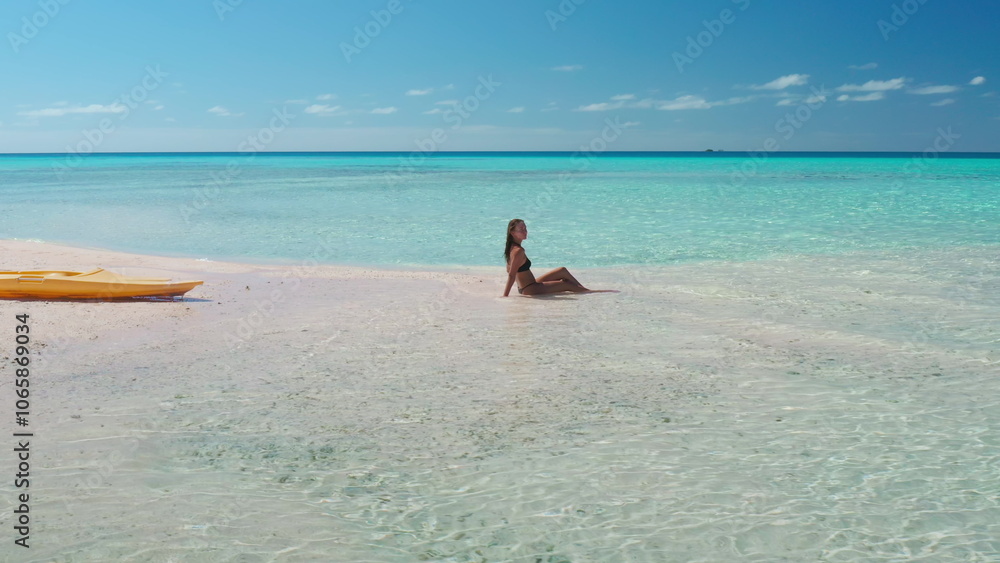 Obraz premium Woman is enjoying the tranquility of a secluded beach, with crystal-clear turquoise water gently lapping at the shore and a kayak resting on the pristine sand