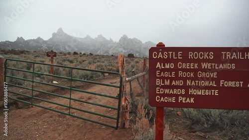 A large red trail sign and gate leading into Castle Rocks State Park, Idaho with a snowstorm in the distance