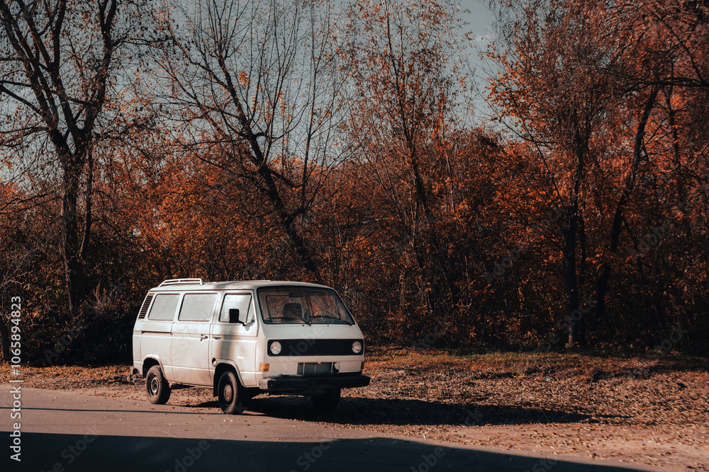 Fototapeta premium Vintage white van parked by a roadside under autumn trees, capturing a nostalgic, travel-ready moment in the fall.