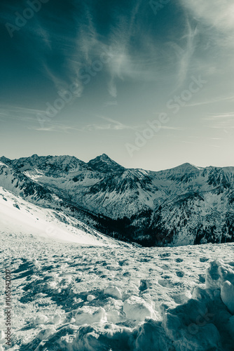 Snow covered slopes descend towards a valley nestled amidst the majestic peaks of the tatra mountains near zakopane, poland, creating a picturesque winter landscape under a vibrant sky