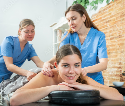 Portrait of a contented young woman lying on a couch in a spa salon, receiving a relaxing massage in four hands photo