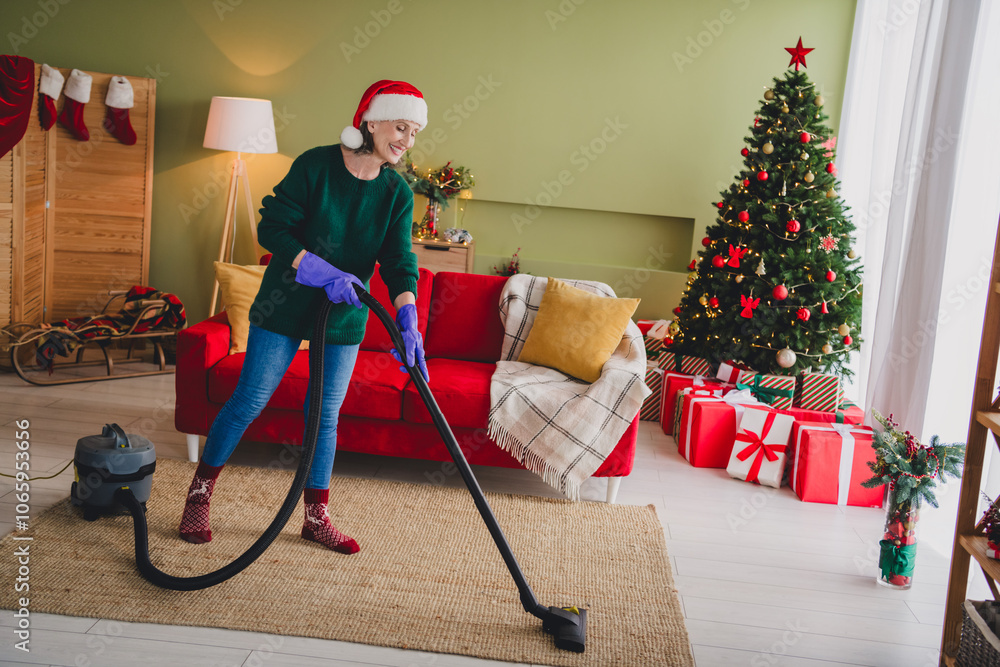 Naklejka premium Photo of charming senior lady wear green clothes cleaning home house indoors vacuuming carpet new year xmas atmosphere