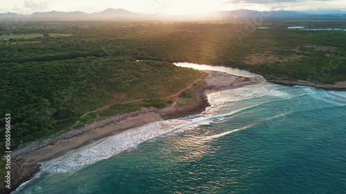 Aerial view of sunset wild tropical coast with golden sand and unspoilt nature Dominican Republic. Breeze rolls onto shore with turquoise ocean waves. Luxurious landscape for relaxing holiday, travel