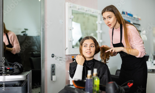 Young confident woman who came to a beauty salon explains to the female hairdresser how she wants to get a haircut photo