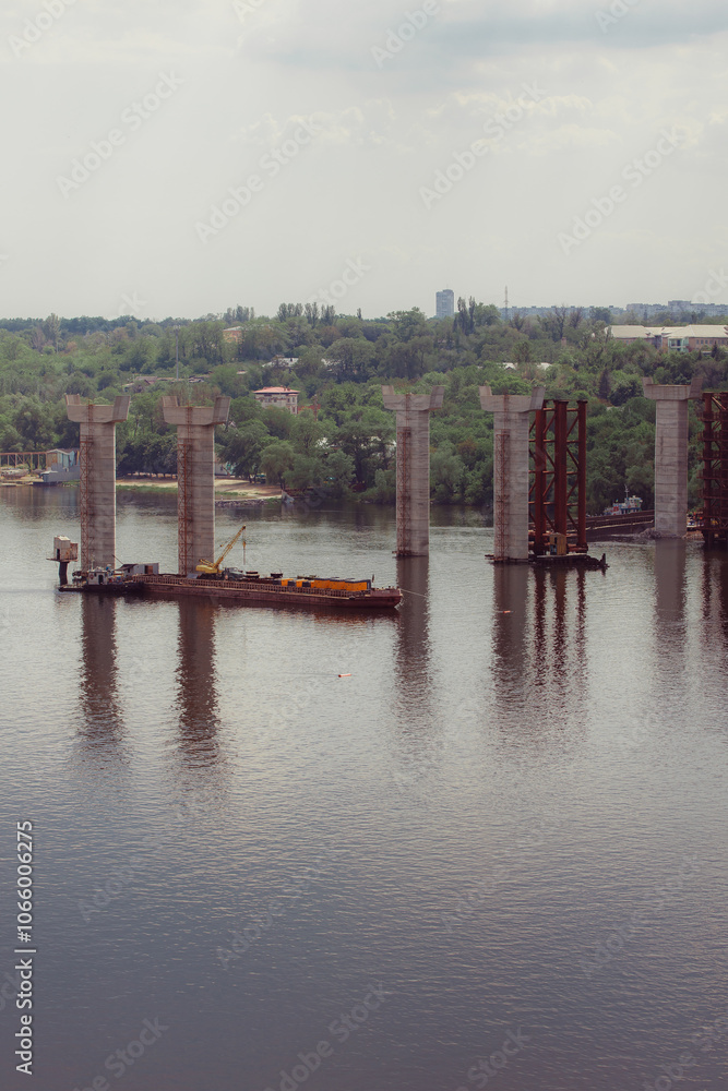 Naklejka premium Concrete bridge over the river. Complex technical projects. A large architectural structure under construction. Temporary iron piles for the construction of columns. Large industrial equipment.