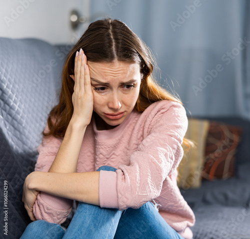 Portrait of a frustrated young European woman sitting on a sofa in an apartment photo