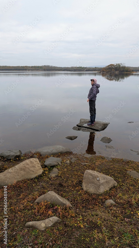 Hiker girl standing on the rock reflected in lake at Coole park nature reserve, County Galway, Ireland, nature background