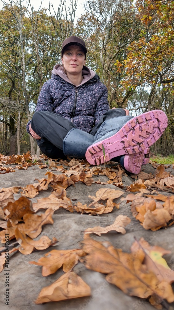 Portrait of beautiful woman in pink rubber boots wellies sitting on the rock and autumn leaves in forest park, nature background