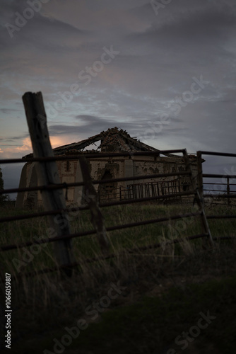 old abandoned dovecote with a partially collapsed roof, set against a dramatic evening sky. The surrounding grass and distant buildings add a rural charm, highlighting the beauty of decay and solitude photo