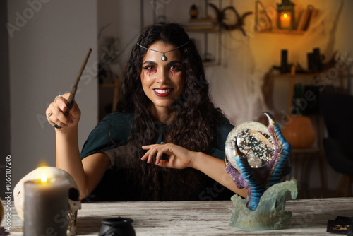 Young witch with magic wand near table at home photo