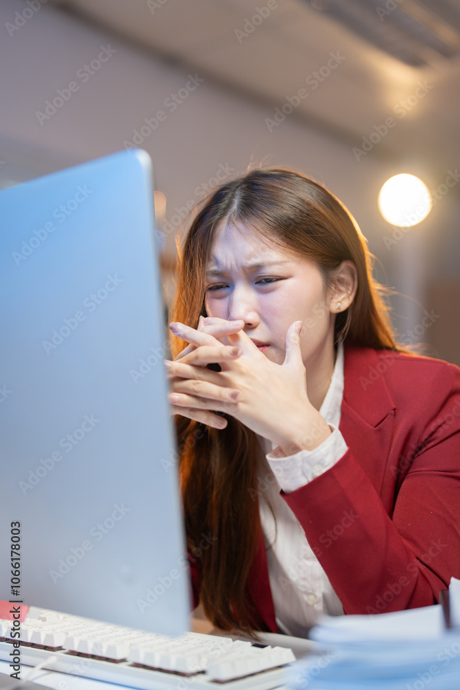 Young asian office worker is having problems at work while looking at her desktop computer, she's covering her mouth with her hands Young asian office worker is having problems at work while looking at her desktop computer, she's covering her mouth with her hands
