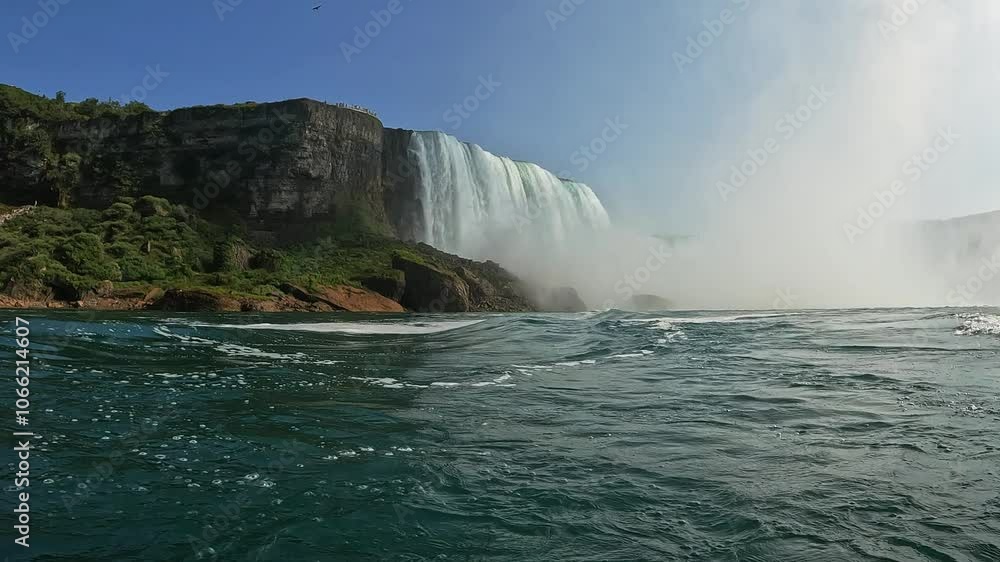 Powerful Niagara waterfall cascades over rocks, creating mist under clear blue skies. Rough water captures the dynamic force of nature. Low-angle water surface moving rear point of view Powerful Niagara waterfall cascades over rocks, creating mist under clear blue skies. Rough water captures the dynamic force of nature. Low-angle water surface moving rear point of view