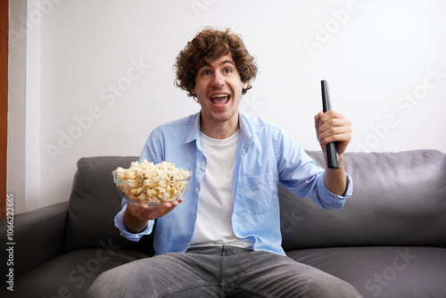 young handsome man watching movies and eating popcorn in a living room #1066222665